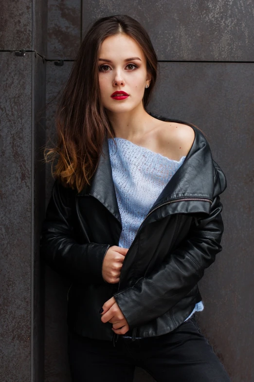 a woman in a black leather jacket leaning against a wall, inspired by Lucia Peka, trending on pixabay, photorealism, red lips, blue outfit, ukrainian girl, wearing shoulder cape