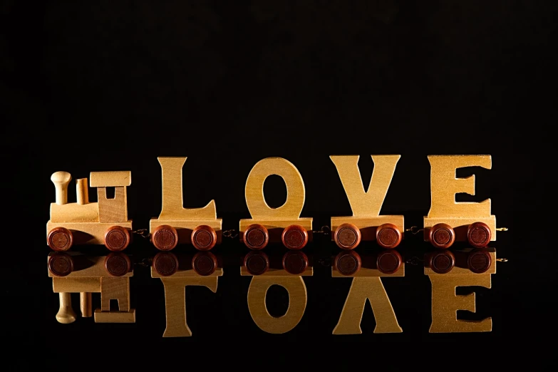 a wooden train with the word love spelled on it, a picture, by Linda Sutton, on black background, gold plated, museum quality photo, on a reflective gold plate