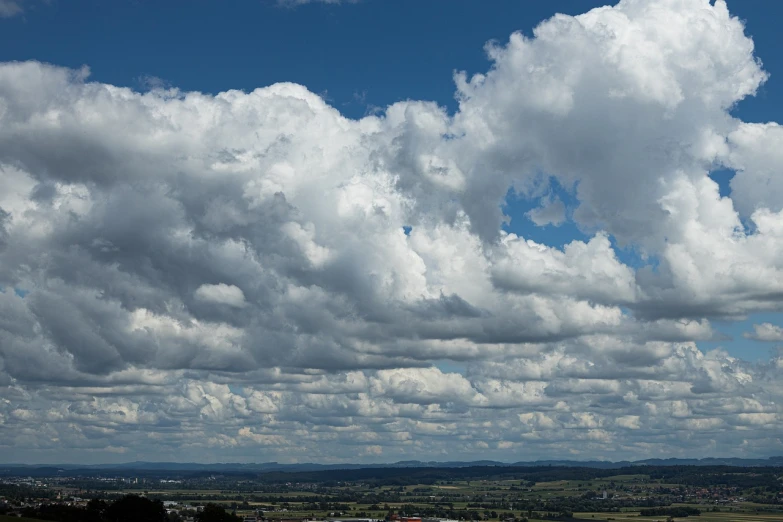 a man flying a kite on top of a lush green field, by Hans Schwarz, big clouds visible, city panorama, day after raining, a dragon made of clouds