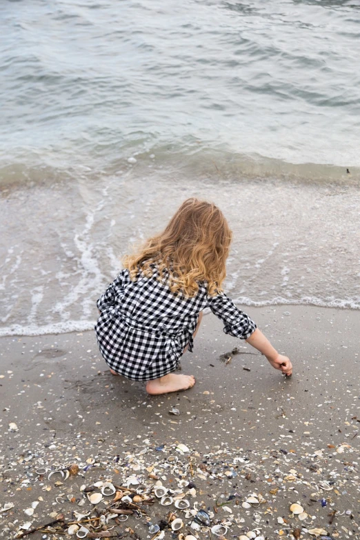 a little girl kneeling on top of a beach next to the ocean, inspired by Vija Celmins, pexels, process art, on a checkered floor, curls, playing with the water, marble!! (eos 5ds r