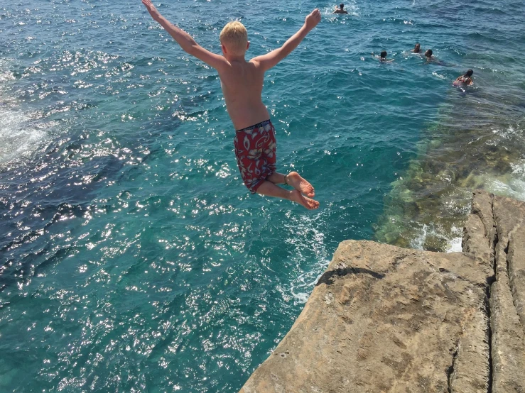 a man jumping off a cliff into the ocean, happening, red haired teen boy, photo taken in 2018, summer swimming party, basil flying