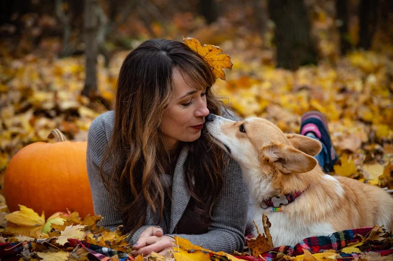 a woman laying on top of a pile of leaves next to a dog, a portrait, by Maksimilijan Vanka, pexels, pumpkin patch, lovely kiss, avatar image, corgi