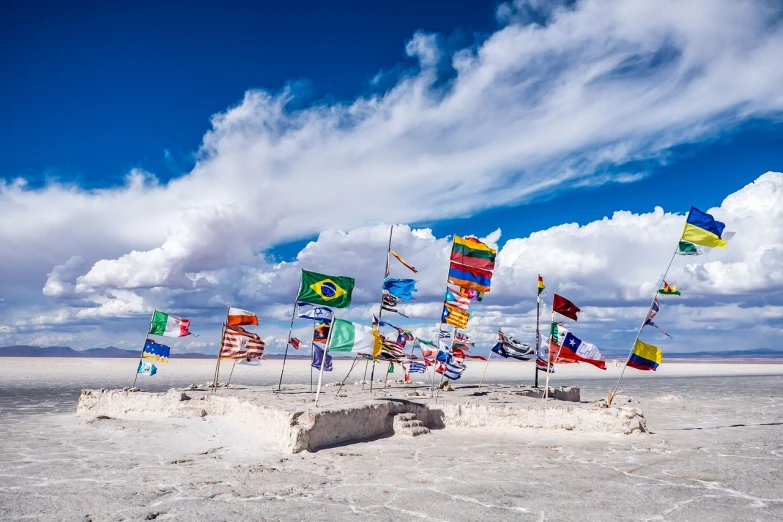 a group of flags sitting on top of a sandy beach, a picture, shutterstock, land art, salt flats with scattered ruins, rich vivid colors, patches of sky, white sand