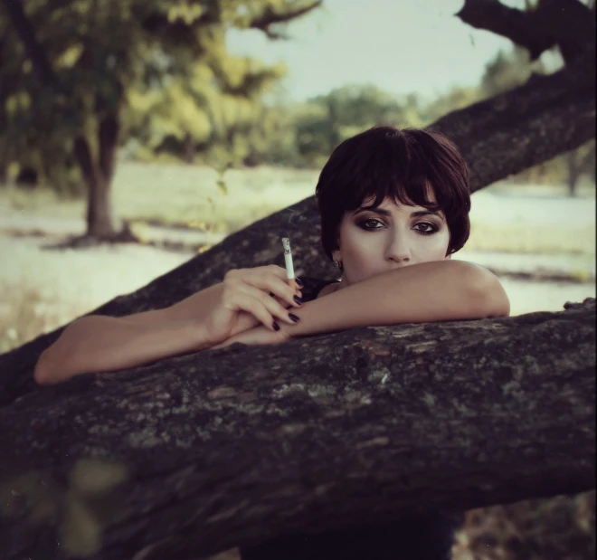 a woman leaning on a tree with a cigarette in her hand, a portrait, unsplash, romanticism, short dark haircut, nadezhda tikhomirova, concept photoset, on a branch