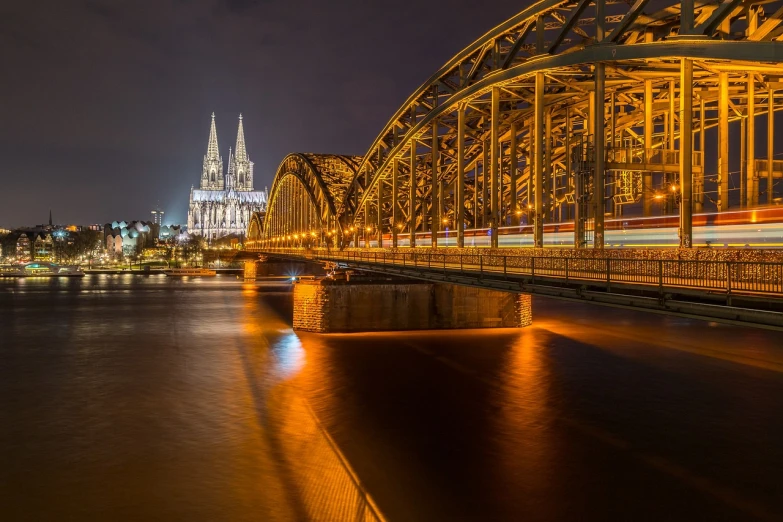 a train crossing a bridge over a river at night, by Karl Hagedorn, shutterstock contest winner, dry archways and spires, shiny gold, germany, cathedral
