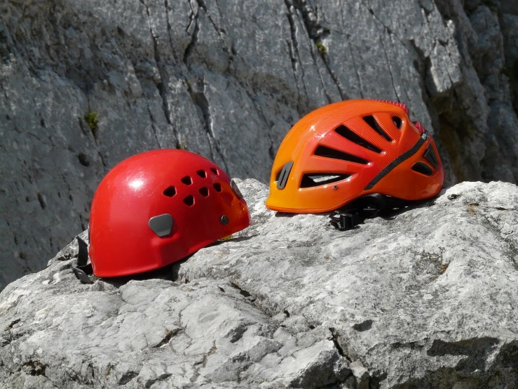 a couple of helmets sitting on top of a rock, figuration libre, belaying, high quality product image”, orange red black white, helmet made of glass