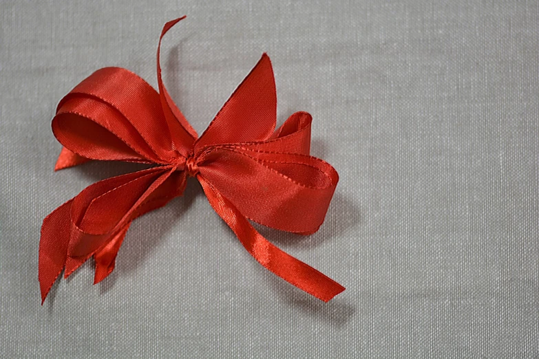 a close up of a red bow on a table, minimalism, on a gray background, linen, very very happy, advanced technique