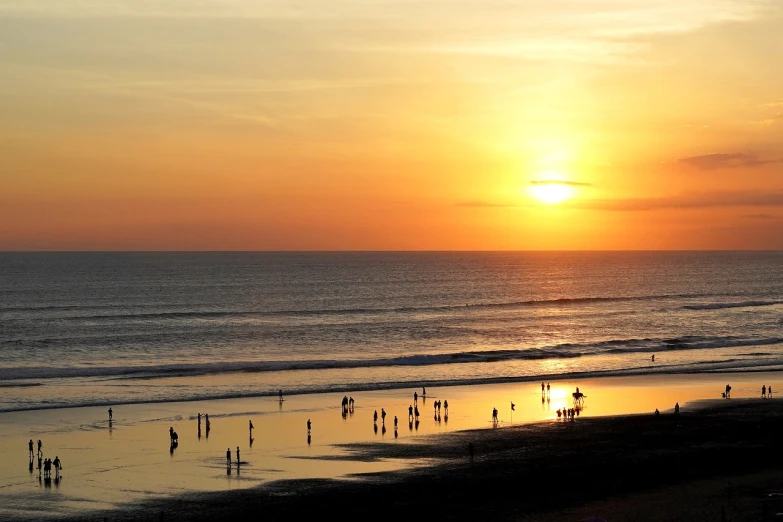 a group of people standing on top of a beach next to the ocean, a picture, by David Burton-Richardson, pexels, minimalism, which shows a beach at sunset, bali, with a bright yellow aureola, omaha beach