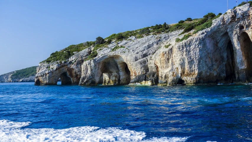 a large rock formation in the middle of a body of water, by Simon Marmion, shutterstock, mediterranean island scenery, beautiful iphone wallpaper, blue white colors, overgrown cave