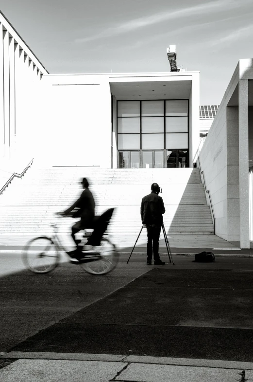 a black and white photo of a person on a bike, a black and white photo, inspired by Henri Cartier-Bresson, unsplash, realism, alvaro siza, two still figures facing camera, at a museum, people at work