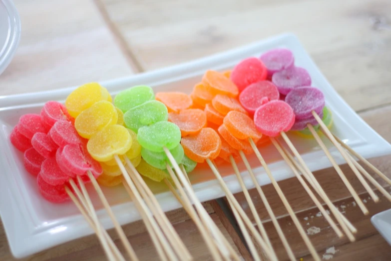 a white plate topped with lots of colorful candies, pexels, pop art, skewer, jelly - like texture. photograph, on a wooden tray, colorful clear sharp focus