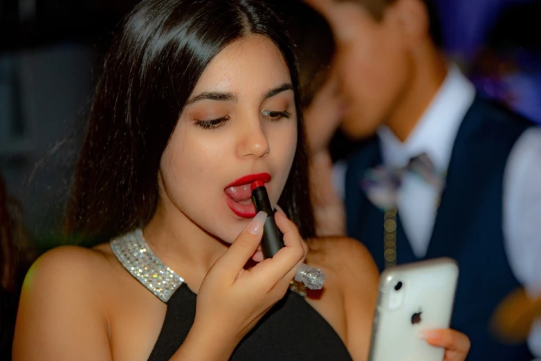 a woman putting on lipstick while looking at her cell phone, a picture, by Amelia Peláez, shutterstock, at the party, isabela moner, black tie, high school girls