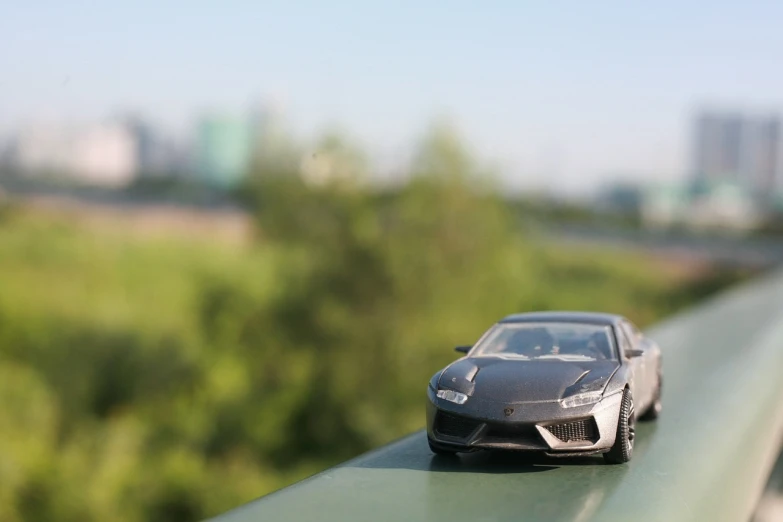 a toy car sitting on top of a green rail, inspired by Bernardo Cavallino, unsplash, photorealism, lamborghini, skyline in back, steel gray body, 5 0 mm bokeh