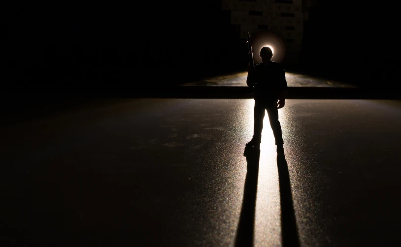 a person standing in the middle of a street at night, a picture, inspired by roger deakins, conceptual art, toy photography, high shadow, flashlight on, warrior fighting in a dark scene
