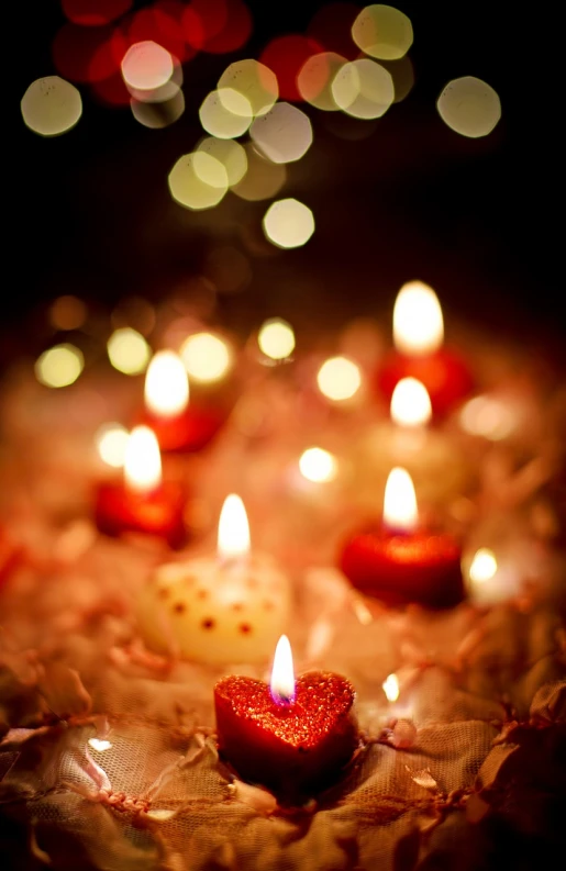 a group of lit candles sitting on top of a table, a tilt shift photo, red hearts, bokeh photo