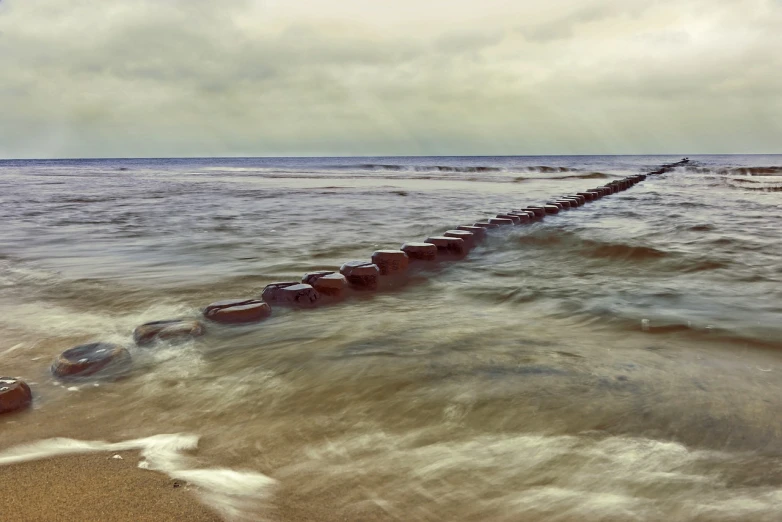 a row of rocks sitting on top of a sandy beach, a tilt shift photo, industrial rusty pipes, violent stormy waters, long exposure photo, watch photo