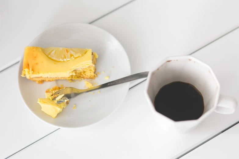 a white plate topped with a piece of cake next to a cup of coffee, by Jan Kupecký, unsplash, minimalism, glossy yellow, self deprecating, split in half, lemonlight