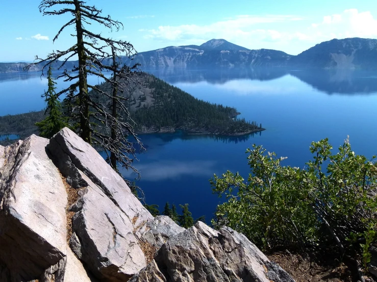 a large rock sitting on top of a mountain next to a lake, a picture, by Linda Sutton, crater lake, usa-sep 20, flora-lush-crater, blue waters