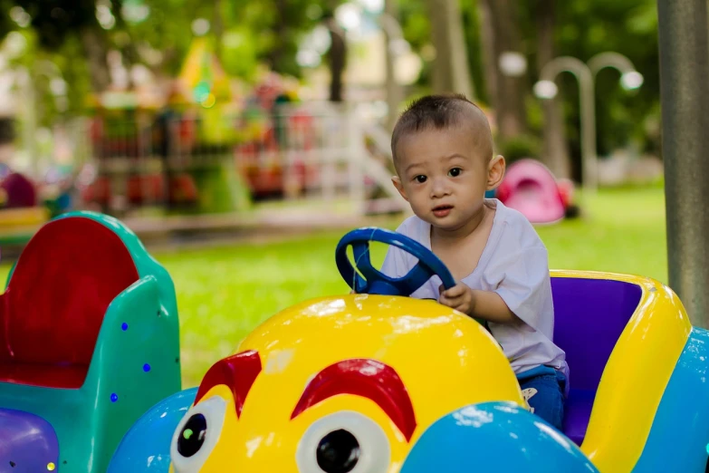 a little boy that is sitting in a toy car, by Bernardino Mei, pexels, park background, square, softplay, full colour