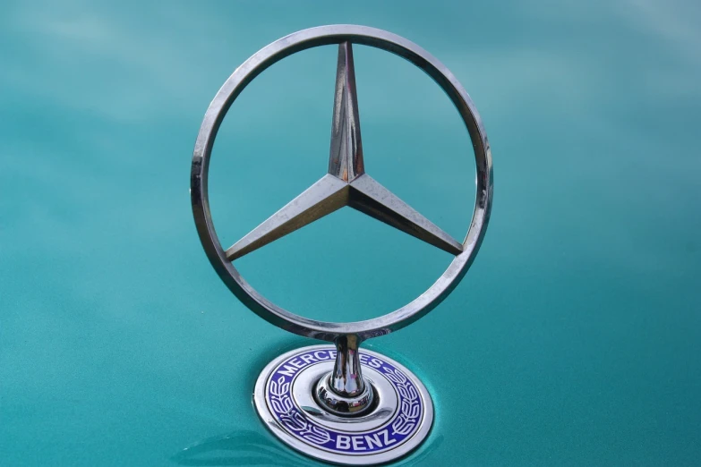 a mercedes emblem on the hood of a car, a picture, by Hans Schwarz, pixabay, arabesque, brand colours are green and blue, taken on a 1960s kodak camera, pentacle, stock photo