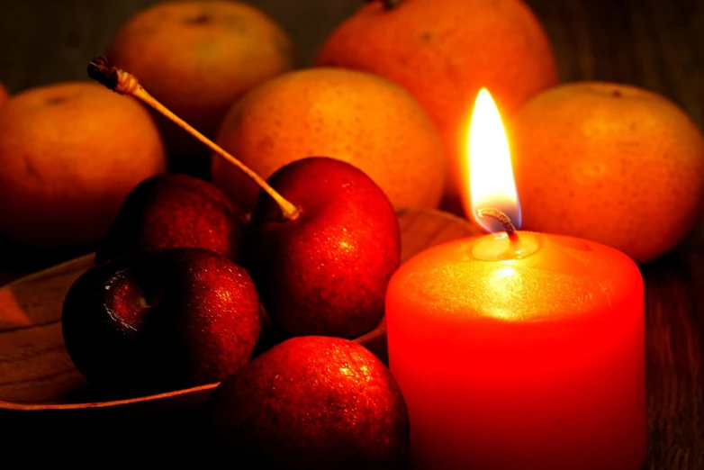 a lit candle sitting next to a pile of fruit, by David Garner, pexels, red and yellow light, cherry, istockphoto, bottom angle