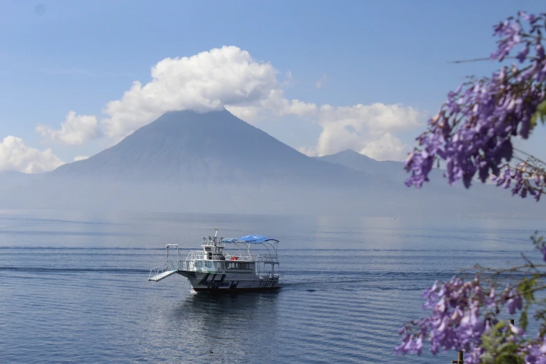 a boat in the water with a mountain in the background, a portrait, flickr, mingei, quetzalcoatl, fuji choko, flowers around, volcanoes in the background