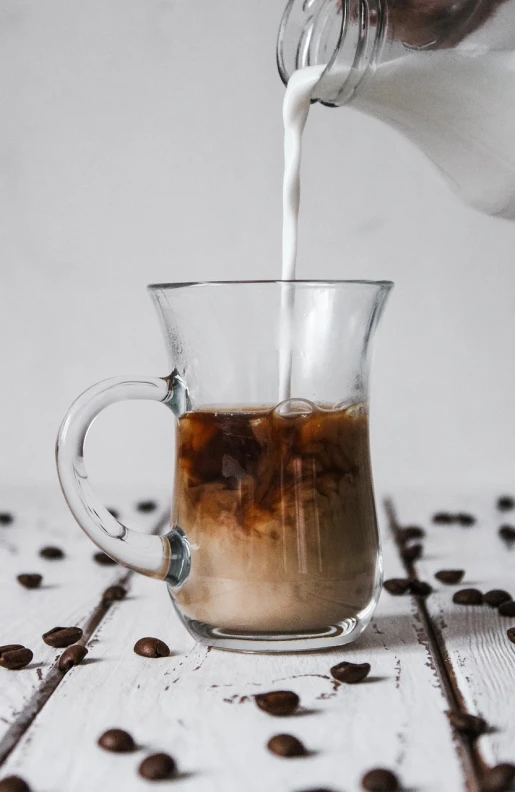 a person pours milk into a cup of coffee, by Emma Andijewska, unsplash, ice coffee, avatar image, marble and wood and glass, on a pale background