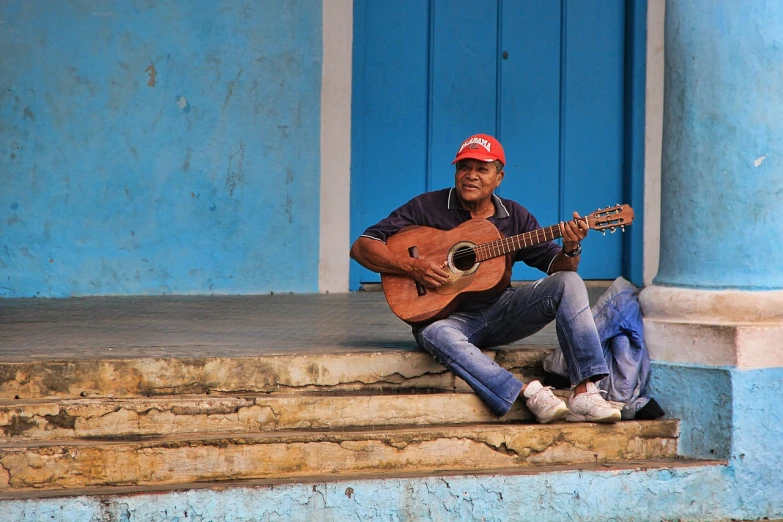 a man sitting on the steps playing a guitar, a photo, by Ramón Silva, flickr, shipibo, posing for a picture, blue and red, joseph moncada