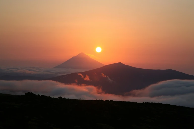 the sun is setting over the mountains above the clouds, by Andrei Kolkoutine, flickr, volcano in the background, two suns, misty, miko