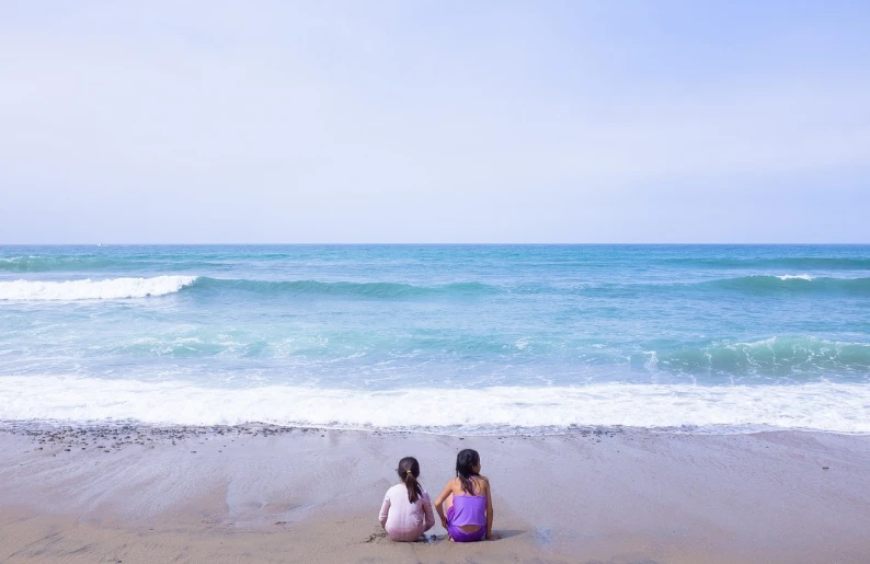 a couple of women sitting on top of a sandy beach, a picture, by Maeda Masao, shutterstock, minimalism, purple water, children, stock photo, marbella