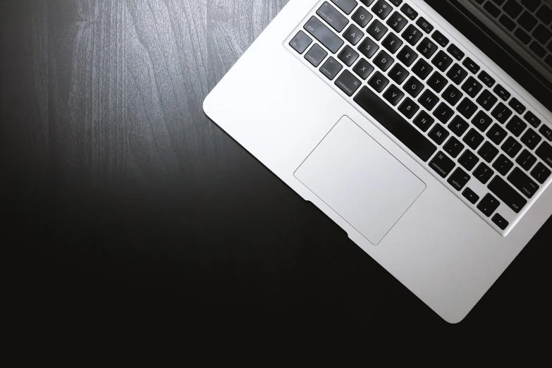 a laptop computer sitting on top of a wooden table, by Robbie Trevino, pixabay, with a black dark background, from above, silver, istockphoto