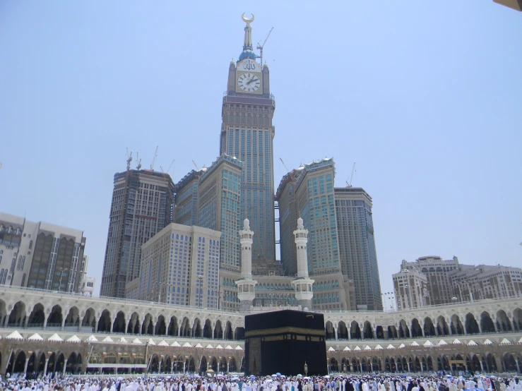 a group of people standing in front of a clock tower, a picture, hurufiyya, also spelled ka'bah or kabah, the building is a skyscraper, very beautiful photo, elevation