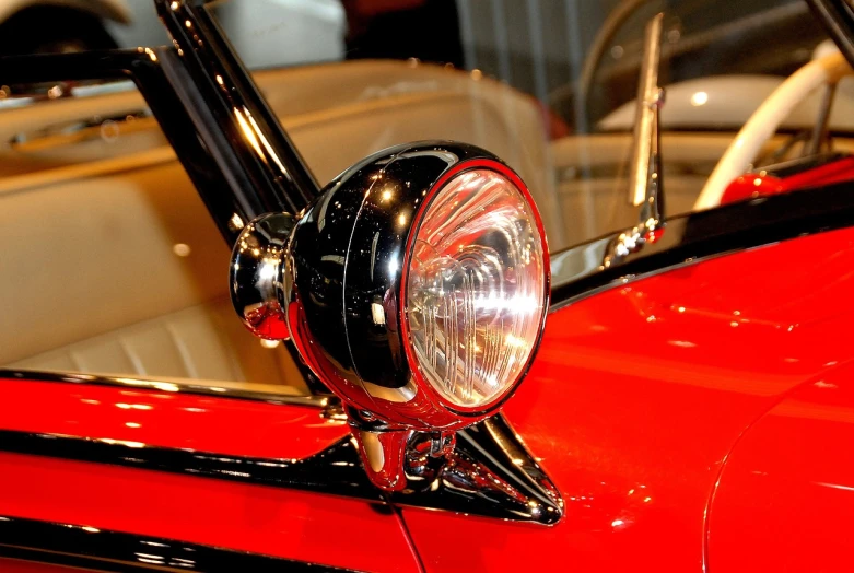 a close up of a red car's headlight, by Dave Melvin, flickr, museum lighting, convertable, red and black color scheme, but very good looking”