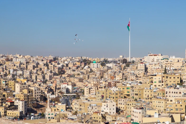 a large city filled with lots of tall buildings, dau-al-set, jordan, red and black flags waving, beautiful sunny day, flying birds in the distance
