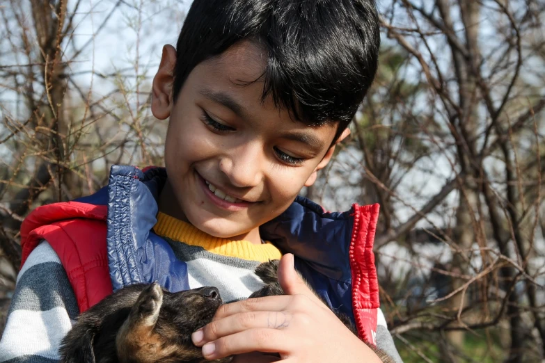 a young boy holding a small dog in his arms, a picture, roshan, spring season, educational, goat