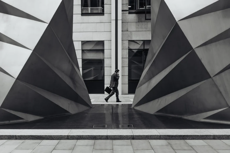 a black and white photo of a man walking in front of a building, by Matthias Weischer, pexels contest winner, modern sculpture, walking to work with a briefcase, geometrical, glasgow