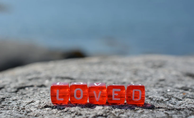 a couple of red dice sitting on top of a rock, a picture, inspired by Dan Luvisi, letters, devoted, love, coveted