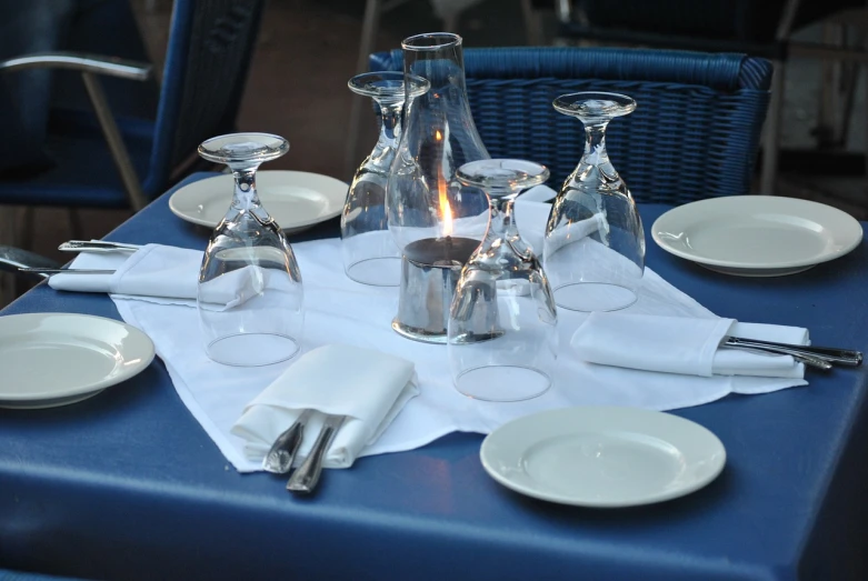 a blue table topped with white plates and silverware, renaissance, summer night, restaurant!, glassware, cuban setting
