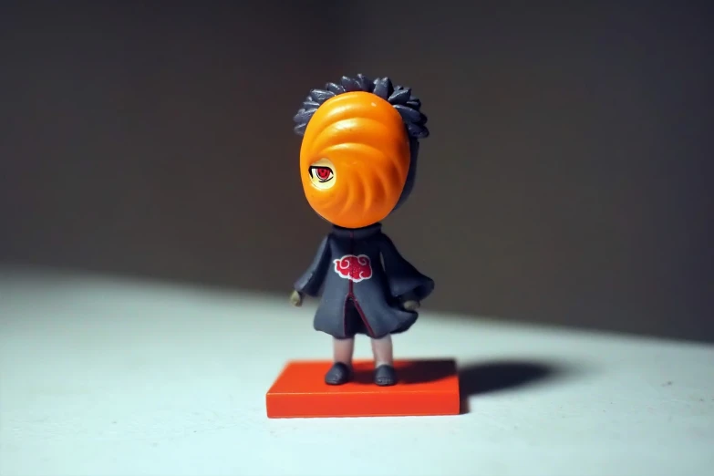 a close up of a small figurine of a person, a picture, inspired by Taiyō Matsumoto, naruto uzumaki, black and orange coat, with a big head, very very low quality picture