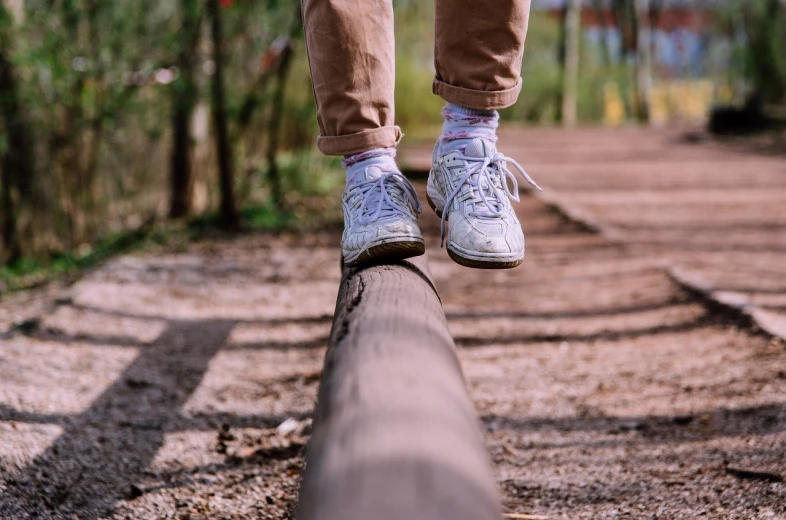a person standing on a log on a train track, trending on pexels, white shoes, horizontally leaping!!!, wooden supports, at a park