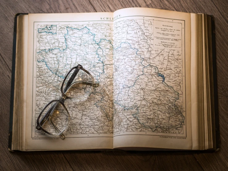 an open book with a pair of glasses on top of it, regionalism, map, zdzisław, old picture, comfortable