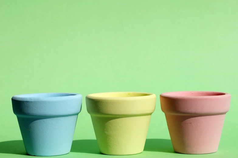 three colorful cups sitting next to each other on a green surface, a pastel, unsplash, pot plants, pastel colorful mold, in a row, eggshell color