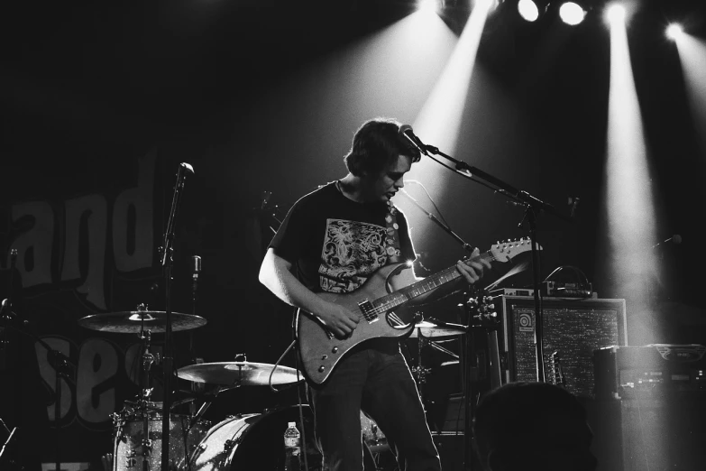 a black and white photo of a man playing a guitar, rex orange county, playing guitar onstage, johnny silverhand, bedhead