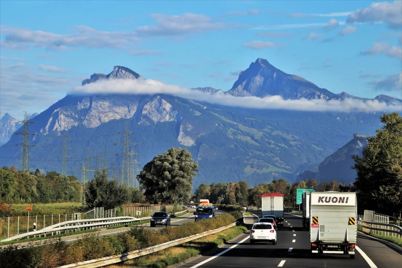 a truck driving down a highway with mountains in the background, a picture, by Oskar Lüthy, flickr, figuration libre, floating mountains, cars on the road, (((mist))), swiss