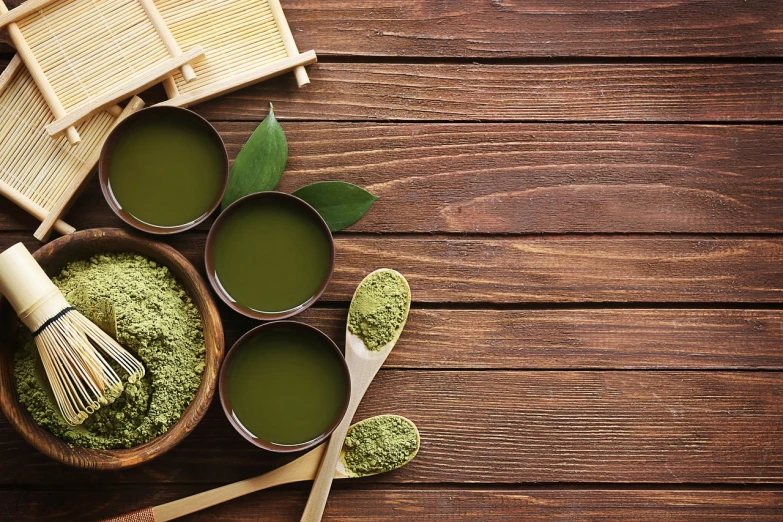 a wooden table topped with bowls of green tea and a whisk, inspired by Asai Chū, trending on pixabay, hurufiyya, skincare, powder, background image, shades of green