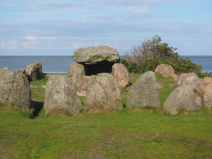 a group of large rocks sitting on top of a lush green field, land art, near the seashore, containing a hidden portal, october, shelter