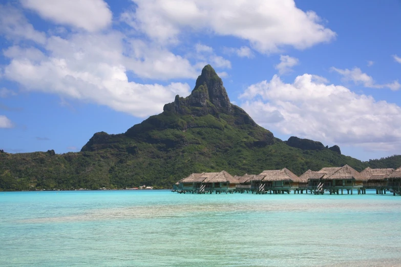 a large body of water with a mountain in the background, a matte painting, polynesian style, telephoto vacation picture, huts, wikimedia commons