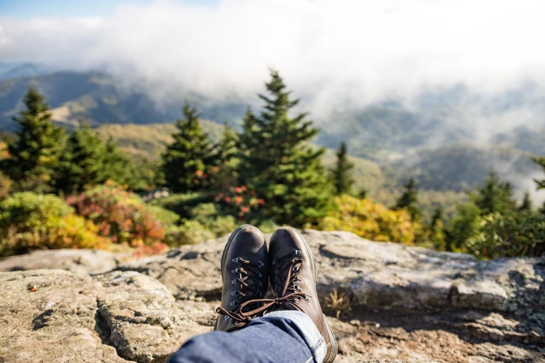 a person's feet on a rock with mountains in the background, inspired by LeConte Stewart, during autumn, low angle photo, relaxing after a hard day, over the tree tops