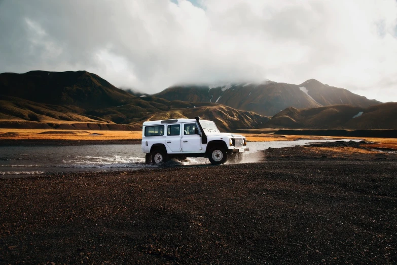 a white jeep driving through a body of water, a picture, by Johannes Voss, pexels contest winner, iceland hills in the background, land rover defender 110 (1985), nostalgic vibes, black sand