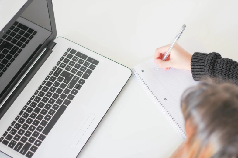 a woman writing on a notebook next to a laptop, a picture, clean and simple, on white paper, console and computer, uploaded